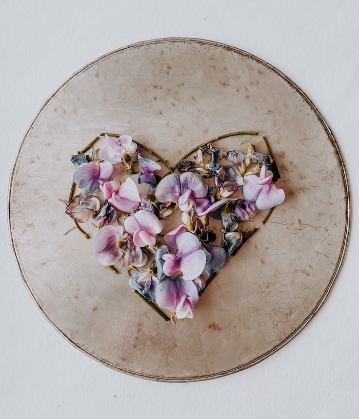services-01 Artistic arrangement of pink and purple petals forming a heart on a vintage round plate, top view.